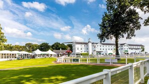 A large, white building with a prominent clock tower, surrounded by a well-maintained lawn and white fences. - Hampton by Hilton Hamilton Park (Hamilton)