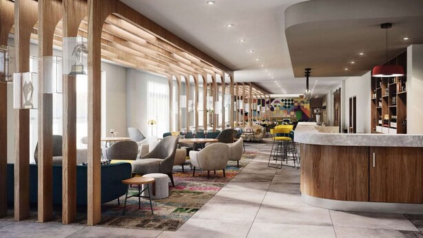 A modern hotel lobby with a curved reception desk, seating areas, and a bar. - Hampton by Hilton Hamilton Park (Hamilton)