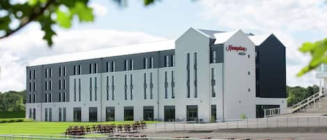 A modern hotel with a prominent 'Hampton' sign, featuring a long, rectangular building with multiple windows and a flat roof.