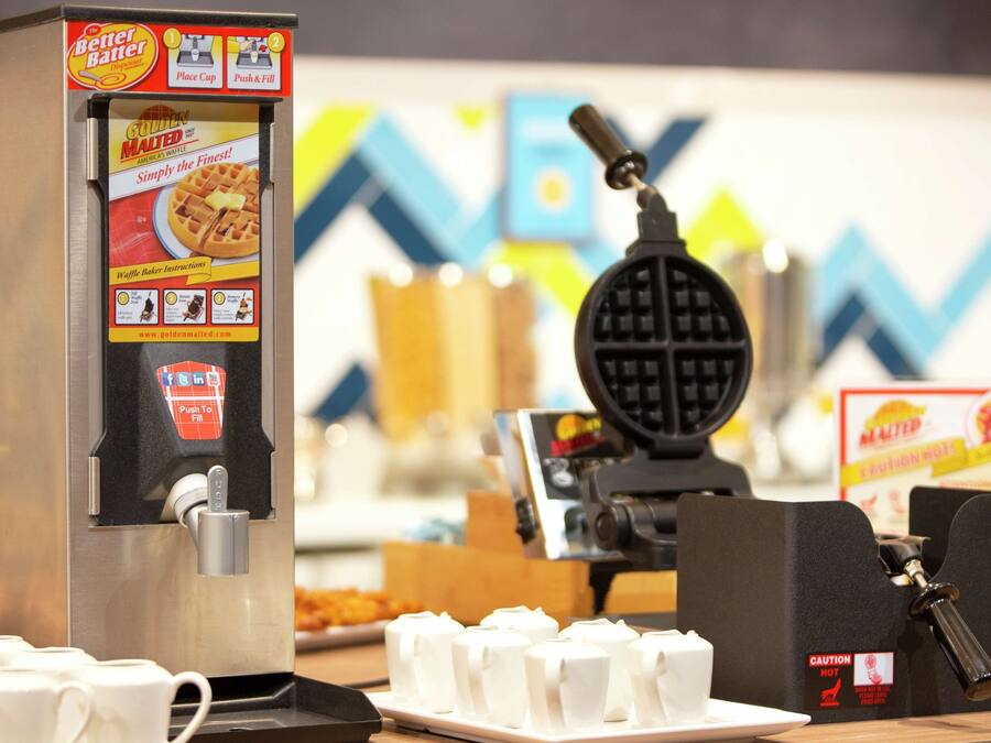 Una piastra per waffle e una macchina per caffè su un bancone con tazze e scatole di waffle.