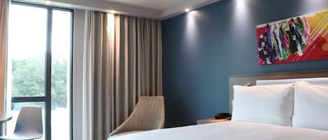 A hotel room with a large bed, a chair, a desk, and a window with curtains.