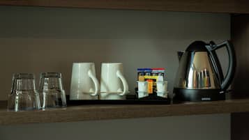 Una repisa con tres vasos transparentes, dos tazas blancas, una cafetera y un montón de sobres de café.