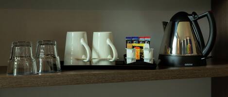 Une étagère avec trois verres transparents, deux tasses blanches, une machine à café et une pile de sachets de café.