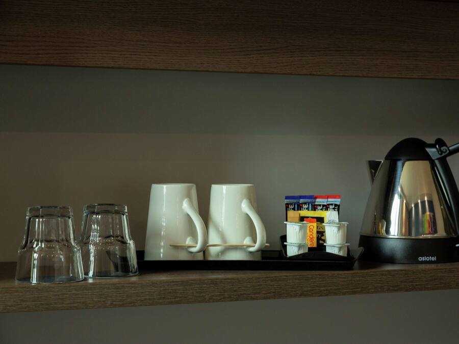 Una repisa con tres vasos transparentes, dos tazas blancas, una cafetera y un montón de sobres de café.