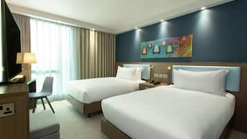 A hotel room with two beds, a desk, a chair, and a painting on the wall.