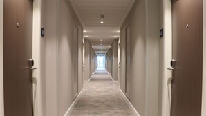 A long, narrow hallway with doors on both sides, leading to a bright area at the end. - Hampton by Hilton Hamilton Park (Hamilton)