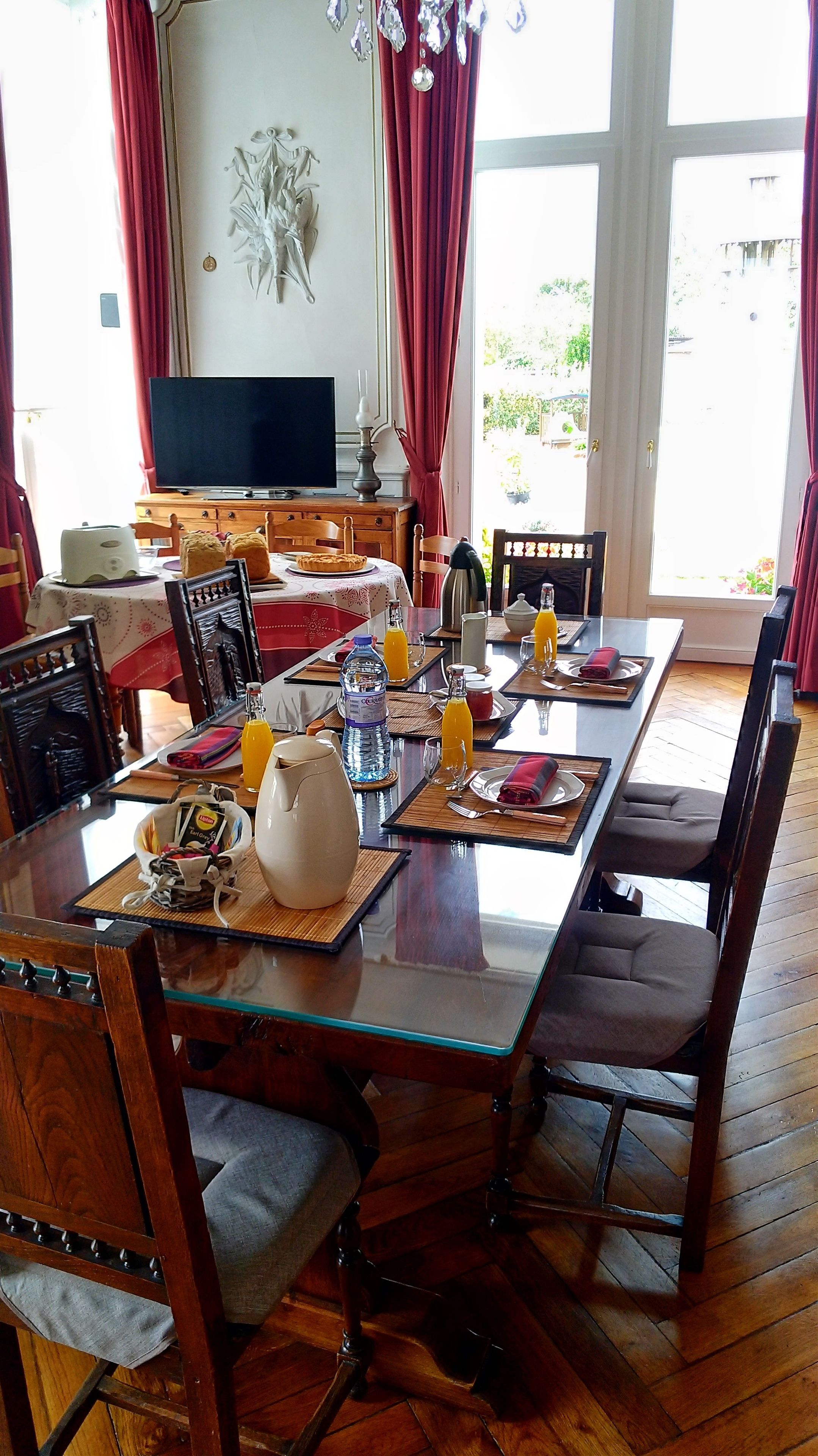 Een eetruimte met een glazen tafel, houten stoelen en een televisie op de achtergrond.