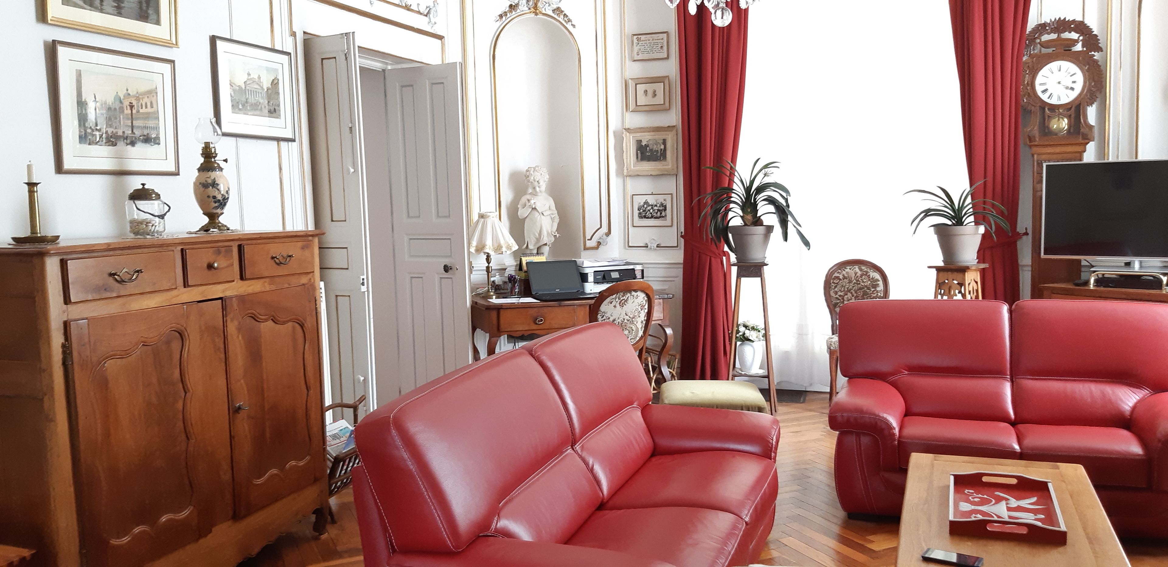 A living room with red leather sofas, a wooden cabinet, a television, and a red curtain.