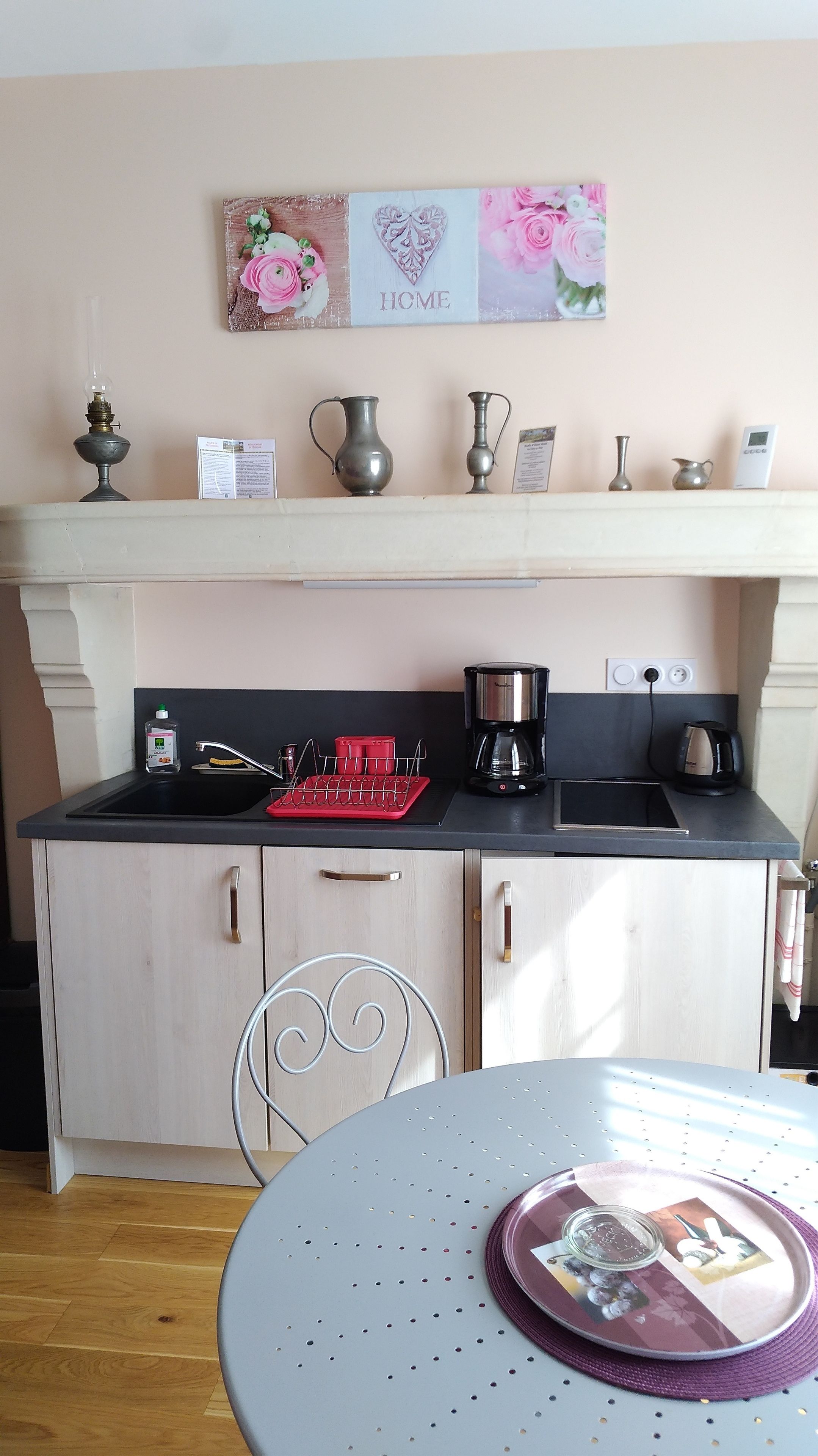 A kitchen with a black countertop, a sink, a coffee maker, and a kettle. There is a shelf above the counter with decorative items and a sign that says "HOME".