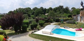 Un patio trasero con piscina, un porche techado y diversas plantas y árboles.