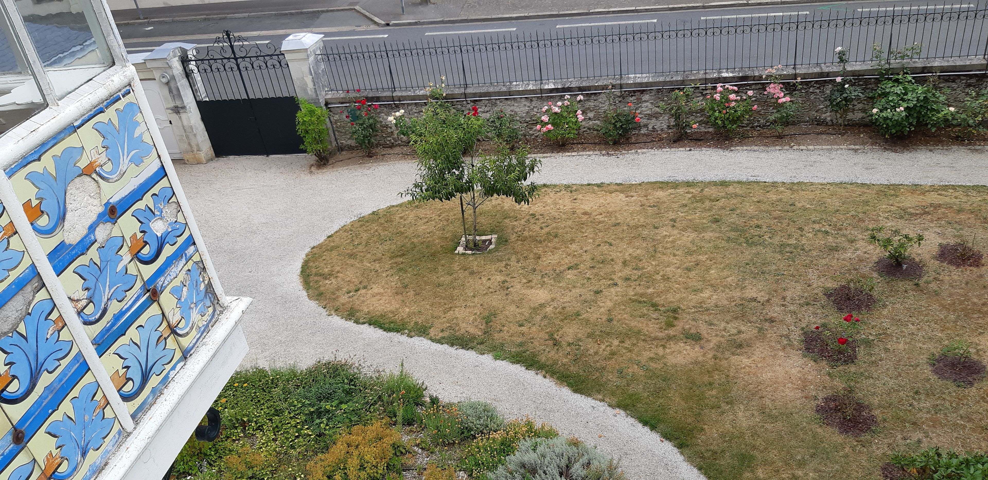 Un patio con un árbol pequeño, un muro decorado y un camino de grava.