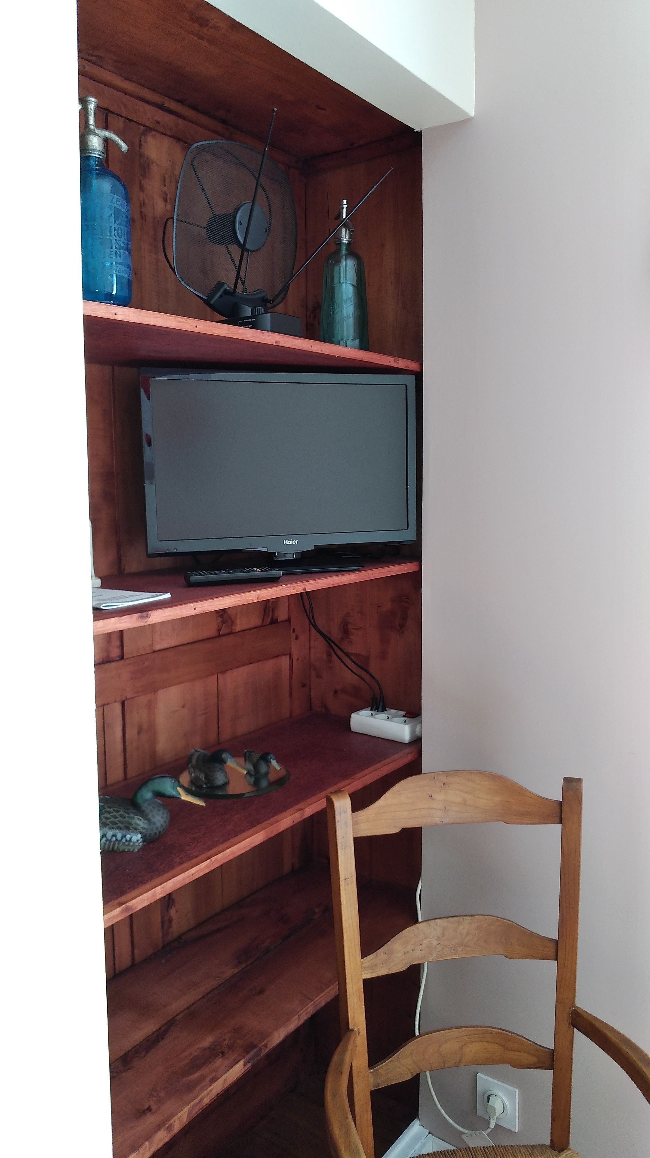 Uma estante de madeira com uma televisão, um ventilador e objetos decorativos.
