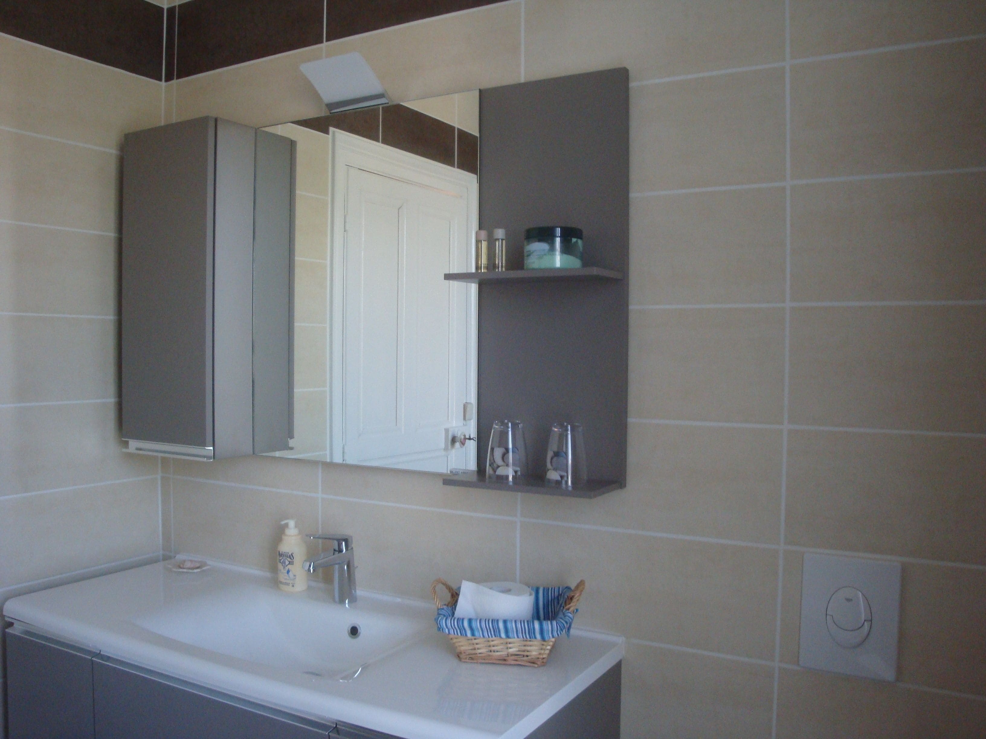 A bathroom with a white sink, a mirror, a towel rack, and a shelf with toiletries.