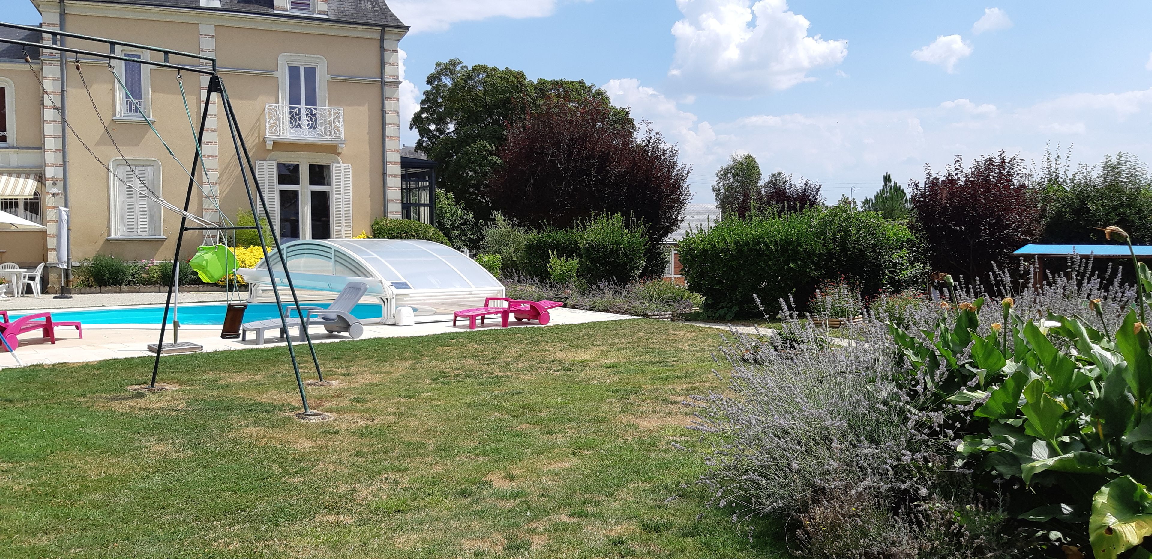 A swimming pool with a glass enclosure, surrounded by a lawn and various plants.
