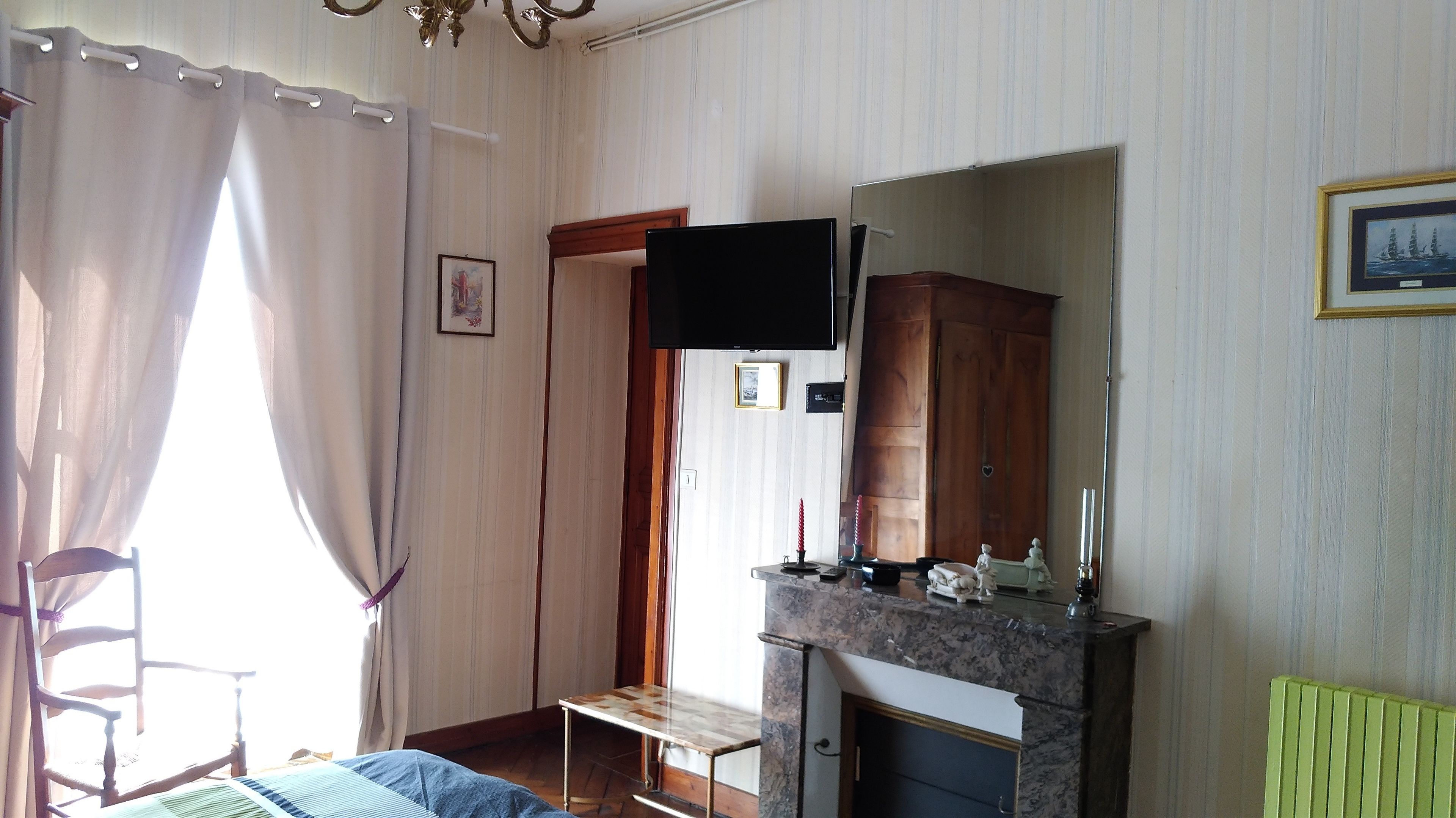 A room with a wooden bed, a fireplace, a television mounted on the wall, and a window with curtains.