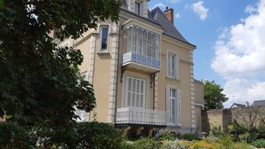 A two-story building with a balcony, a stone wall, and a garden with various plants and flowers. - Chambres d'Hôtes Les Clefs du Bonheur (Chateau-Gontier)