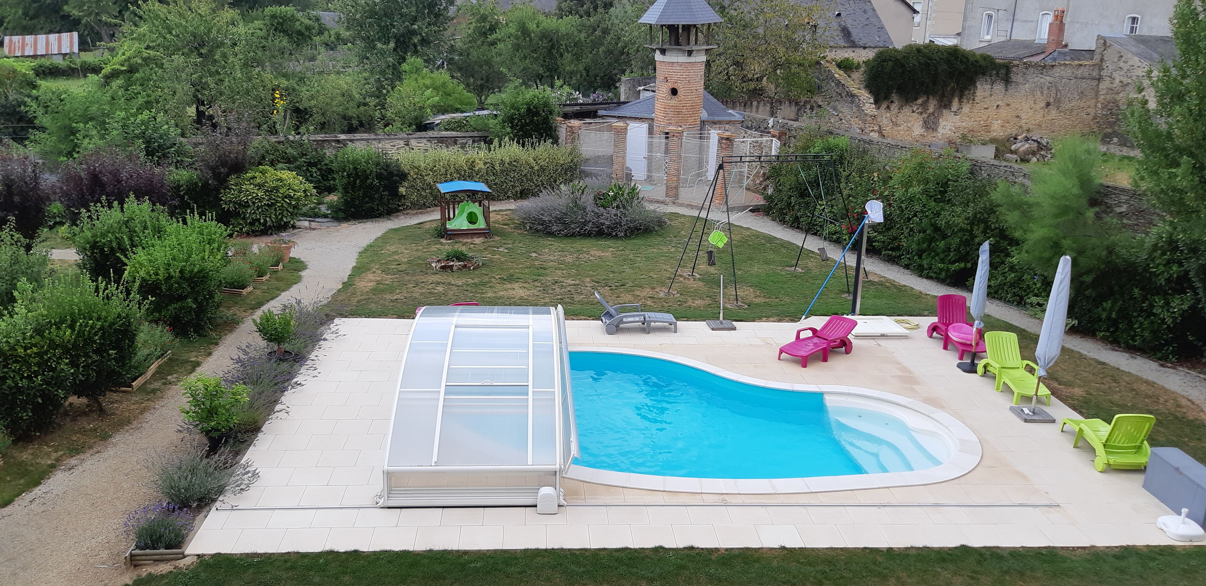 En swimmingpool med et nedsænket spabad, omgivet af en terrasse med liggestole og en lille legeplads.