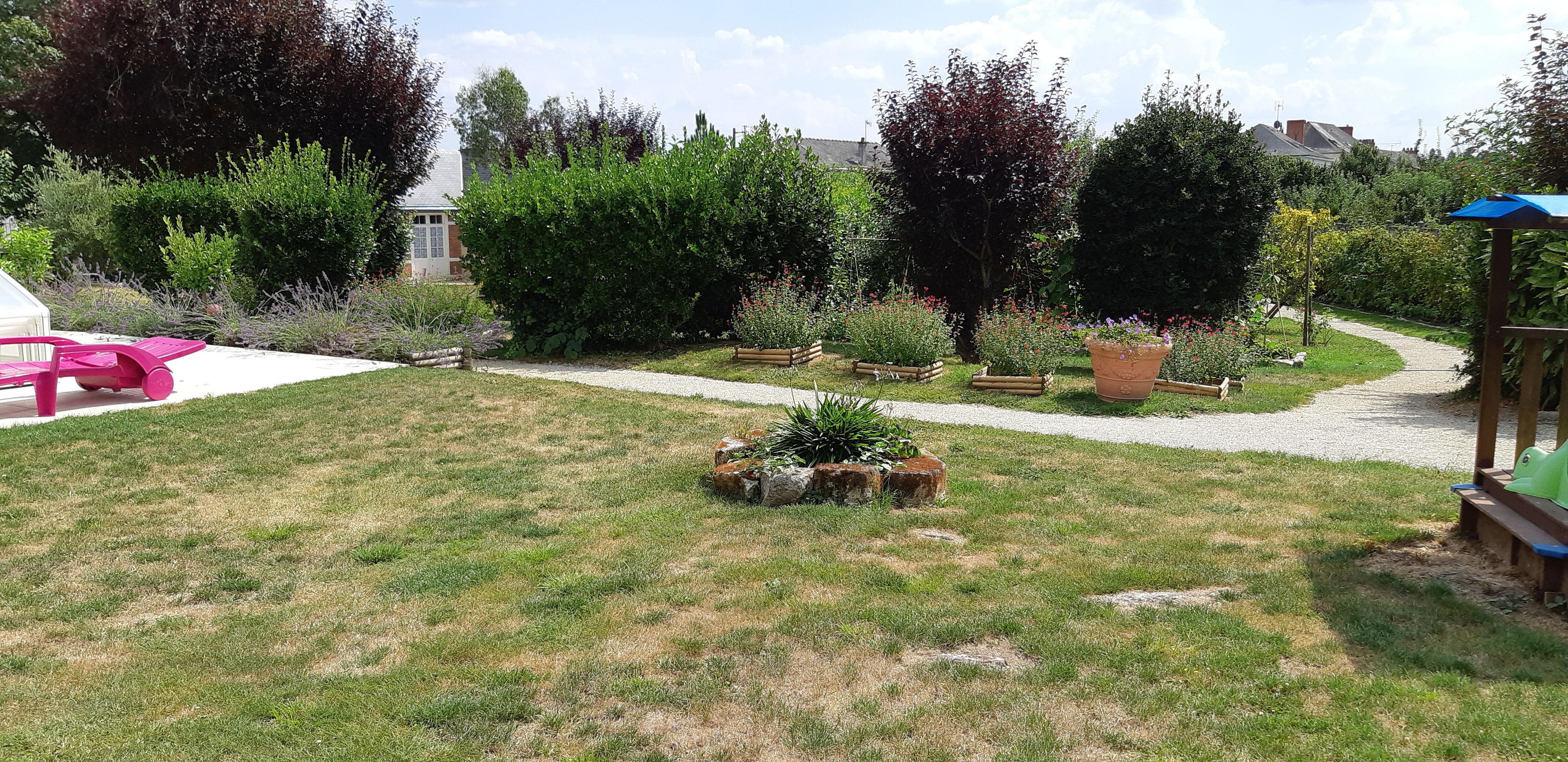 A garden with a gravel path, wooden planters, and a pink chair.