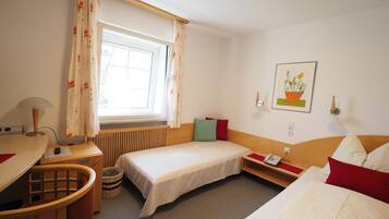Ein Hotelzimmer mit einem Bett, einem Schreibtisch, einem Stuhl, einem Telefon und einem fensterbepflanzten Fenster.