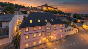 Un bâtiment rose doté de nombreuses fenêtres et d’une entrée centrale, entouré d’une rue pavée et d’autres immeubles d’habitation.