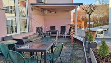 Eine Terrasse im Freien mit Tischen und Stühlen, einer kleinen Sitzecke und Topfpflanzen.