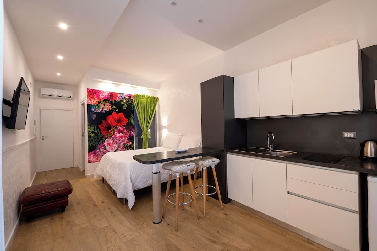 A compact kitchen with white cabinets, a black countertop, and a small bar stool.