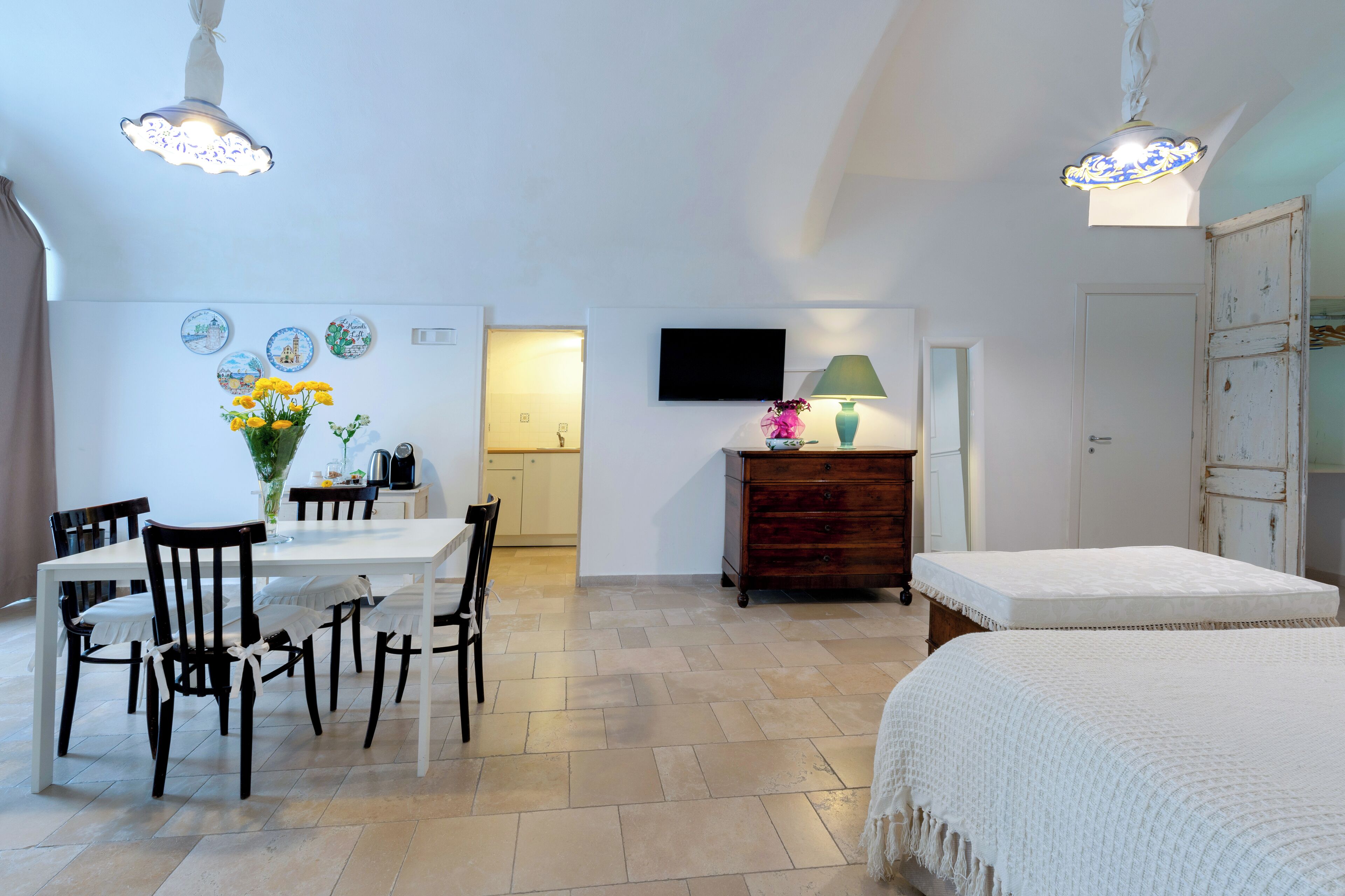 A room with a dining table, chairs, a TV, a dresser, and a bed.