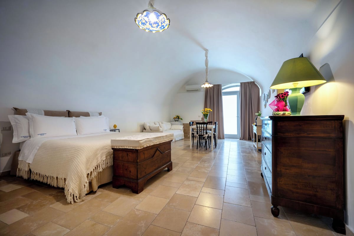 A bedroom with a bed, a wooden dresser, a table with chairs, and a hanging light fixture.