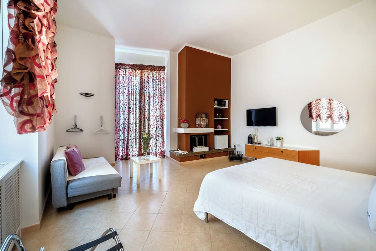 A hotel room with a bed, a sofa, a desk, a TV, and a bathroom.