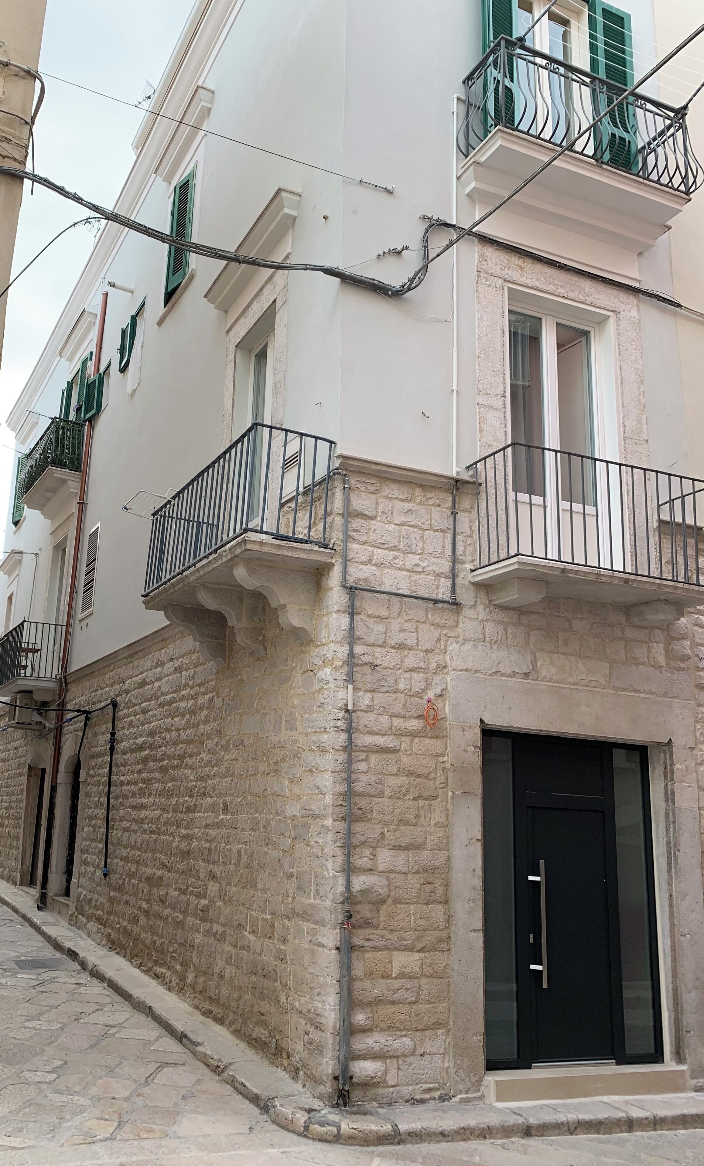 Un edificio con fachada de piedra, balcones con barandillas de metal y una puerta negra.