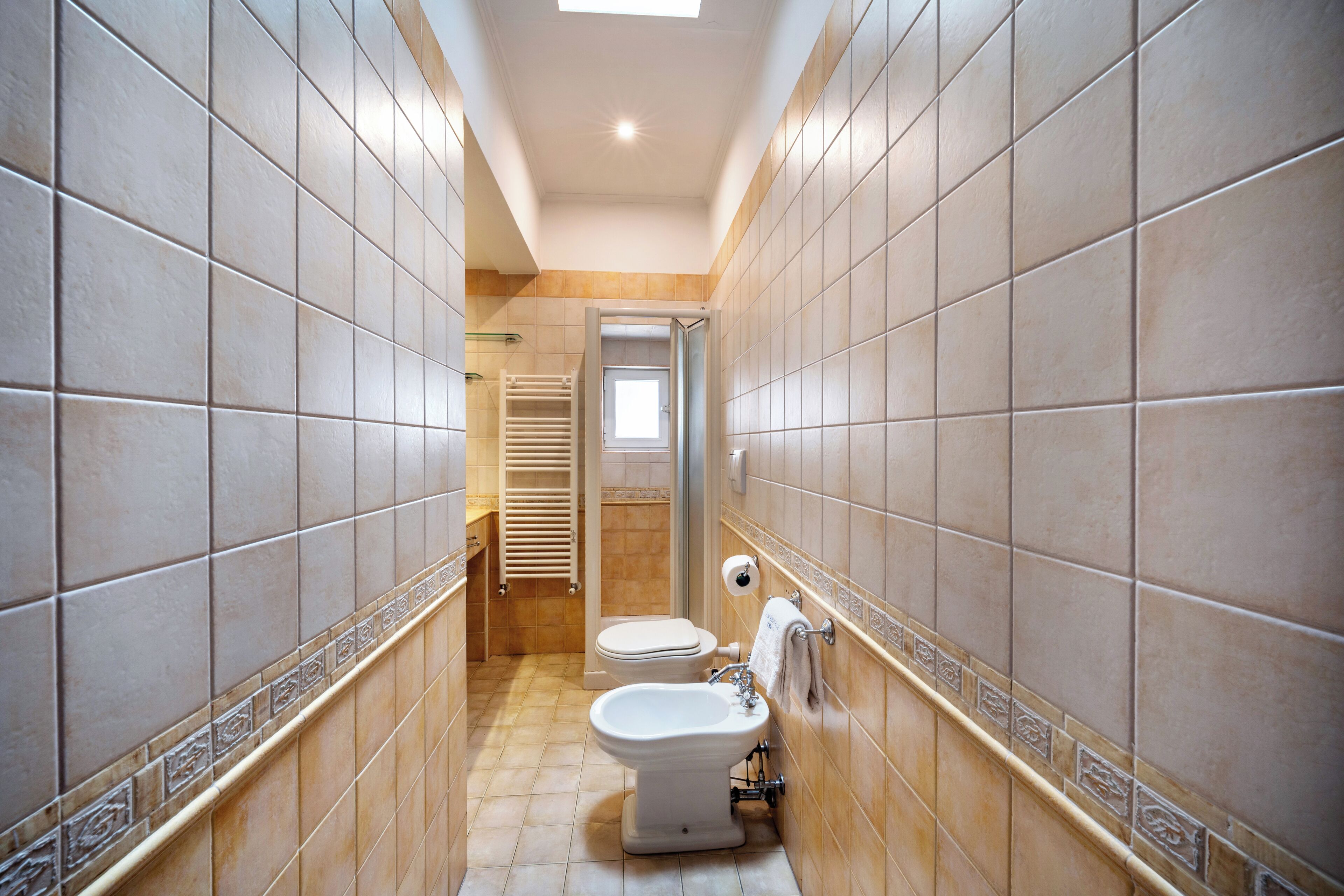 A narrow bathroom with two toilets, a bidet, and a towel rack.