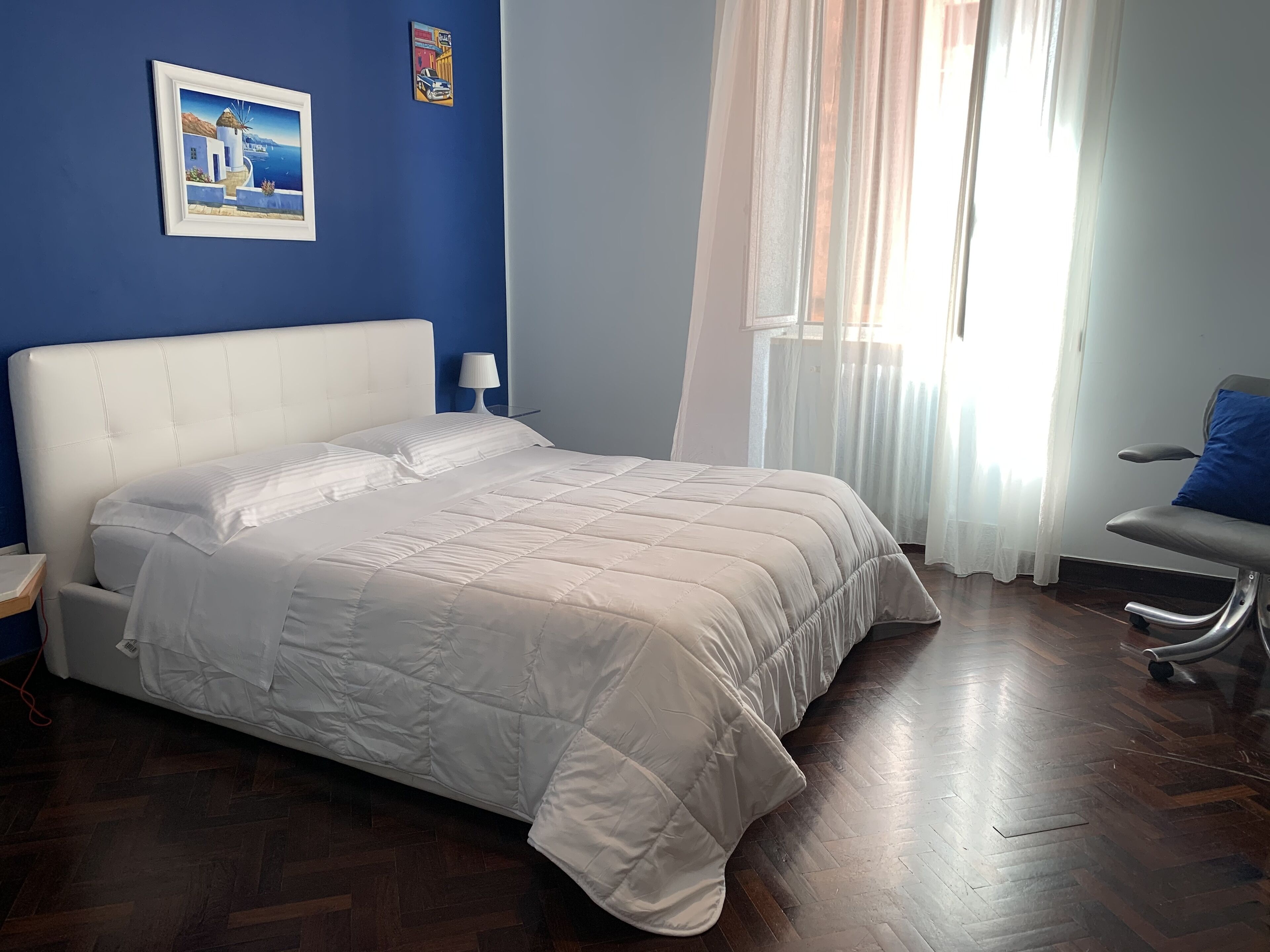 A neatly made bed with a white duvet, a bedside lamp, and a chair with a blue cushion.