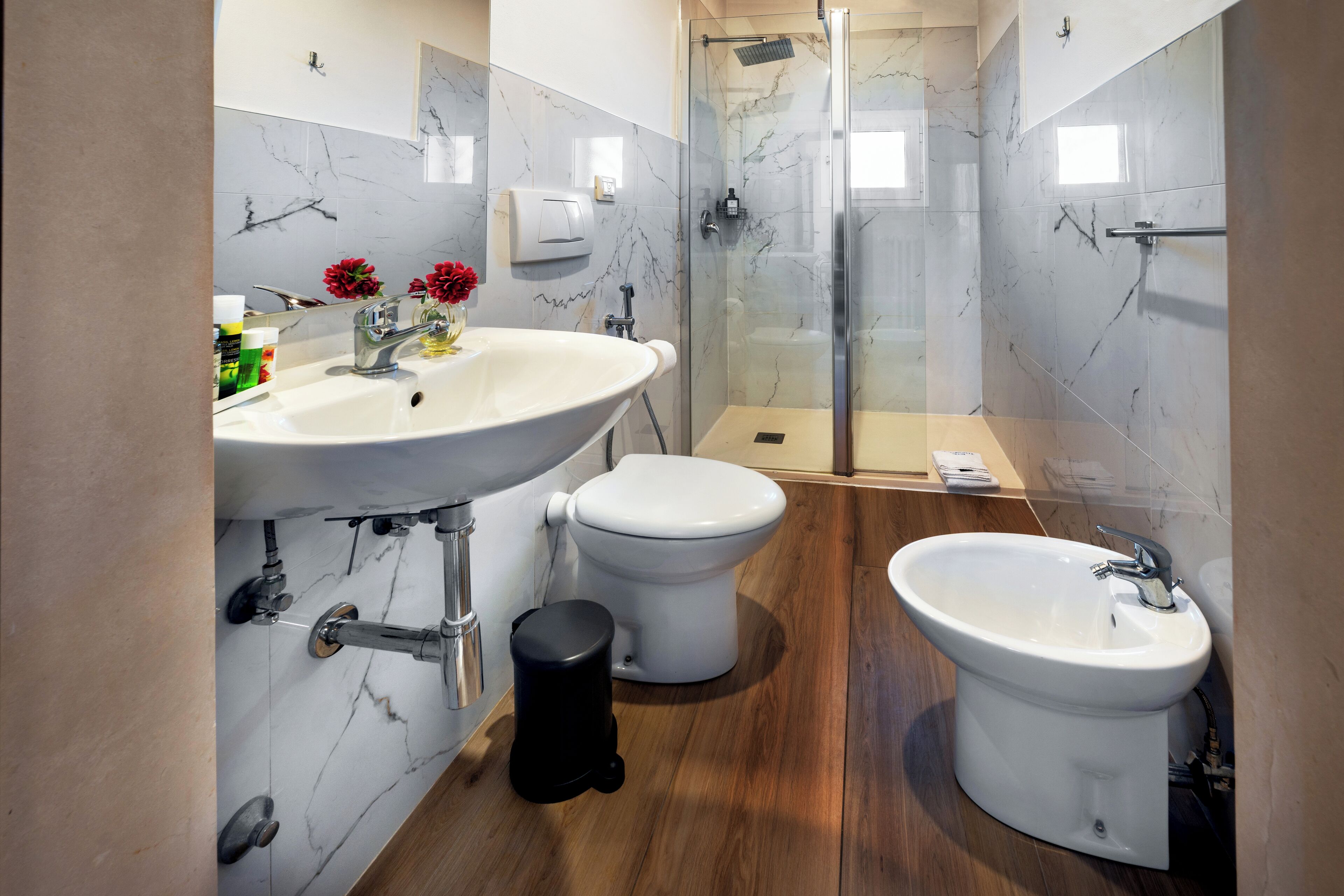 Un baño moderno con un lavamanos grande, dos inodoros, un bidé y una ducha con mampara de vidrio.