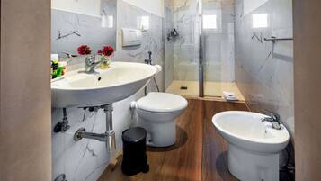 Un baño moderno con un lavamanos grande, dos inodoros, un bidé y una ducha con mampara de vidrio.