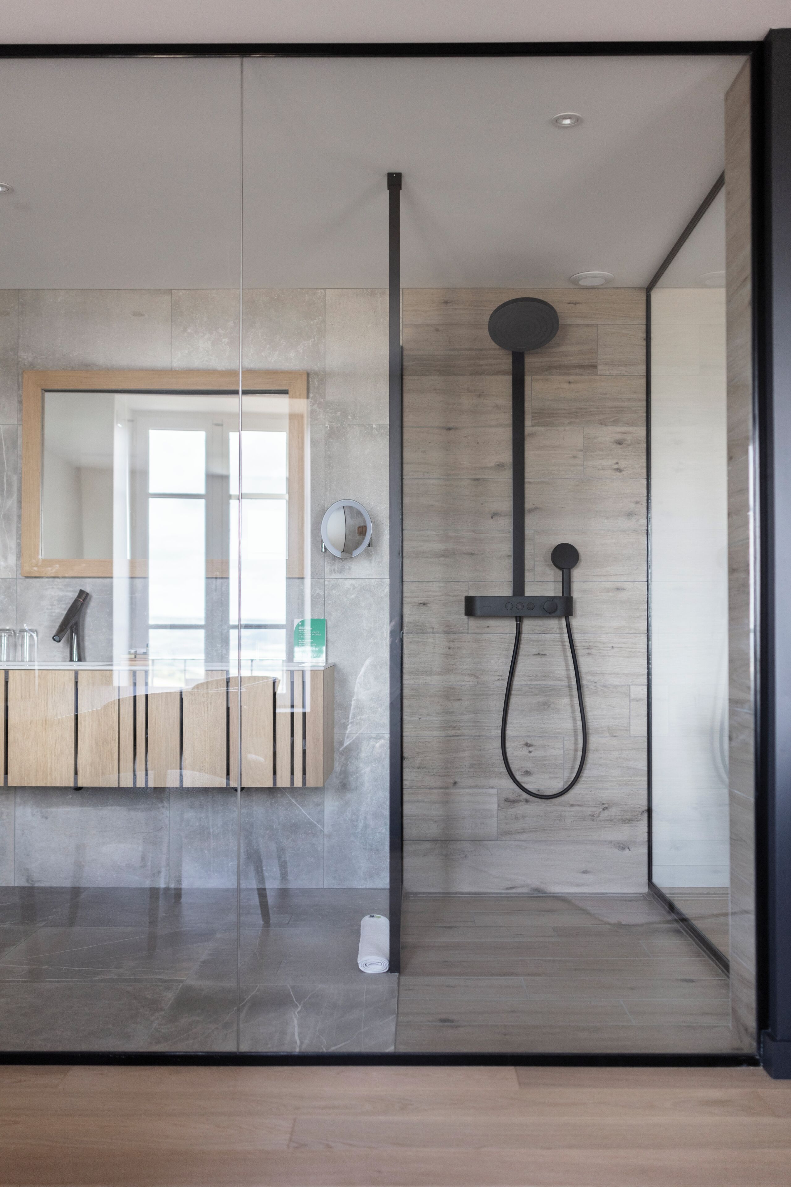 Une salle de bain moderne avec une douche à parois de verre, un meuble-lavabo en bois et un grand miroir.