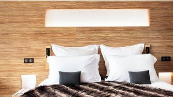 Una habitación de hotel moderna con cabecera de madera, una cama grande con almohadas blancas y oscuras, un plaid de piel y lámparas de noche.