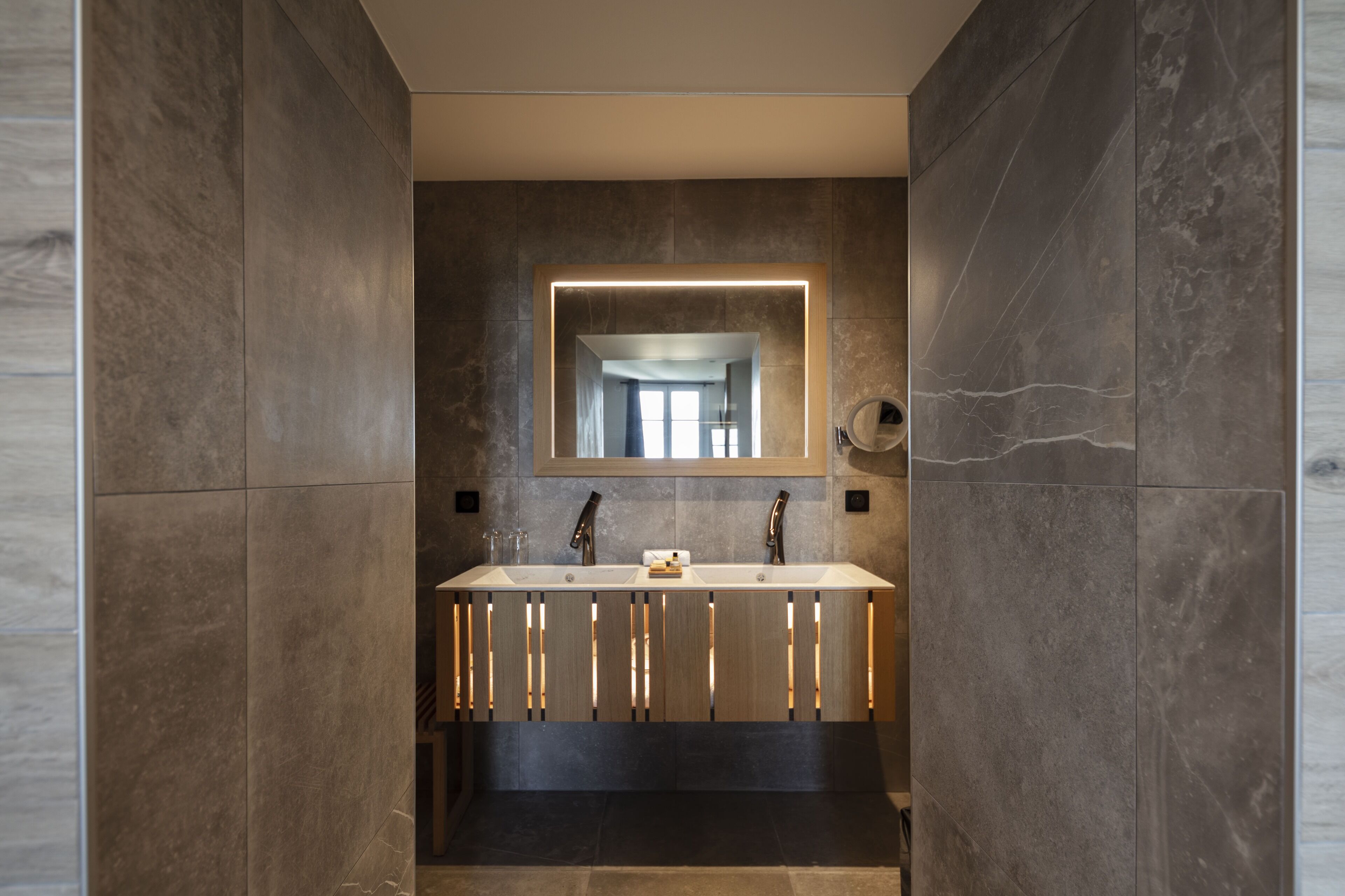 Un baño moderno con un espejo grande, dos lavamanos y un piso oscuro.