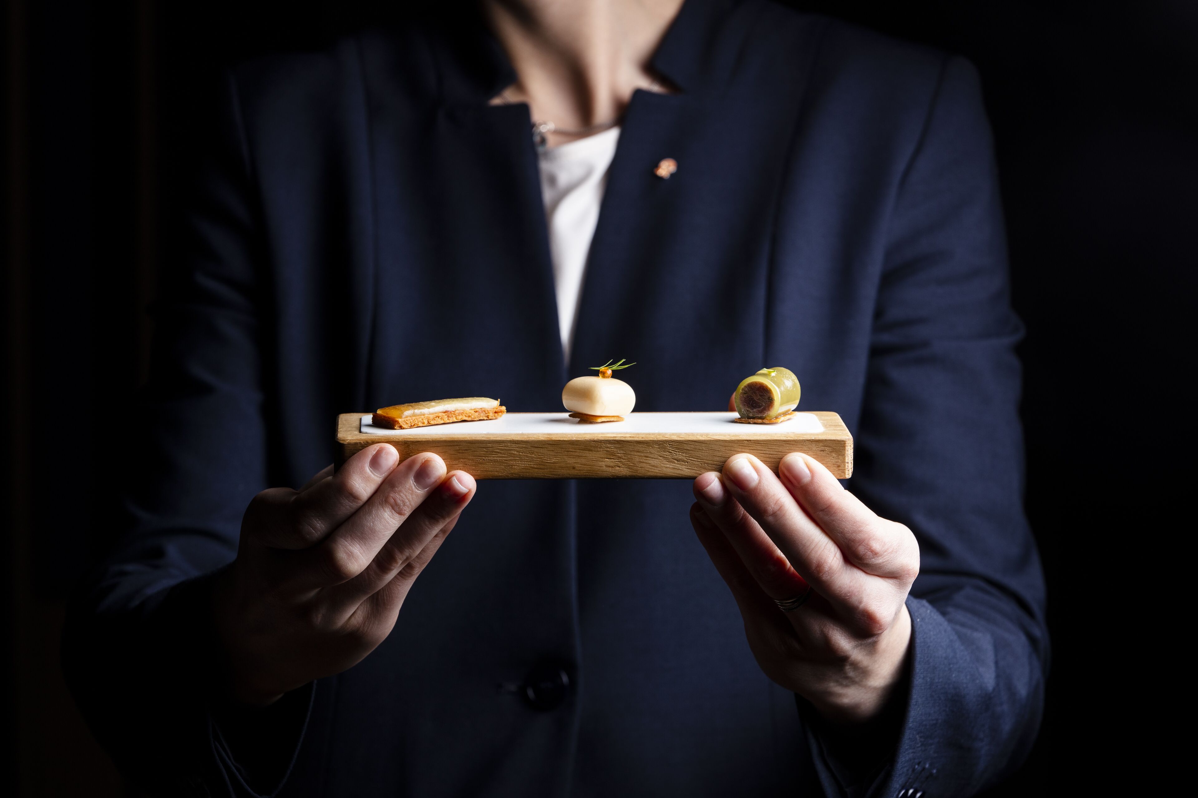 A person holding a wooden tray with three small food items.