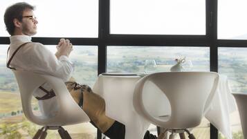 A man seated at a table with a view of a landscape through large windows.