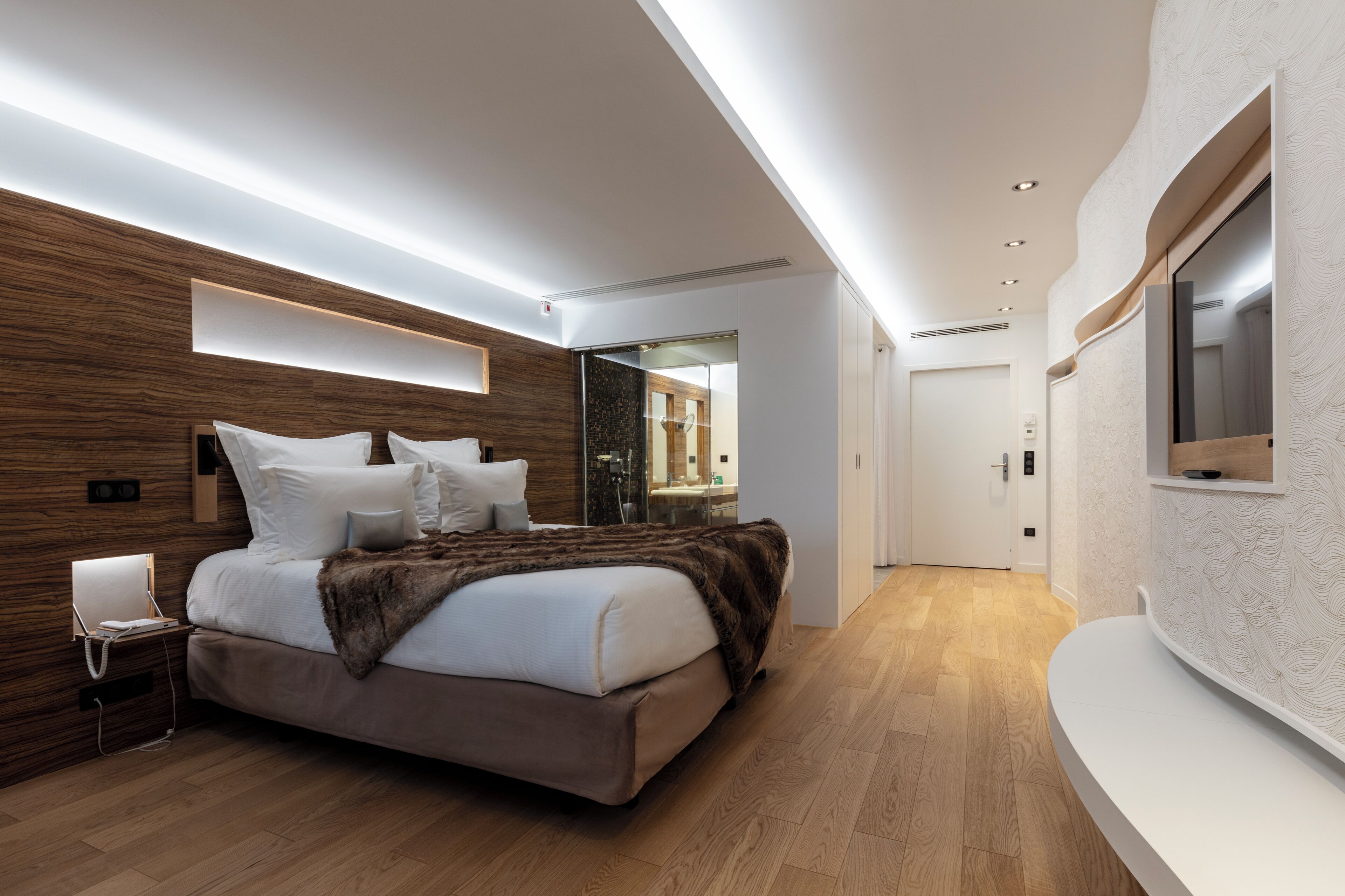 Un dormitorio moderno con cama, mesita de noche y televisor montado en la pared.