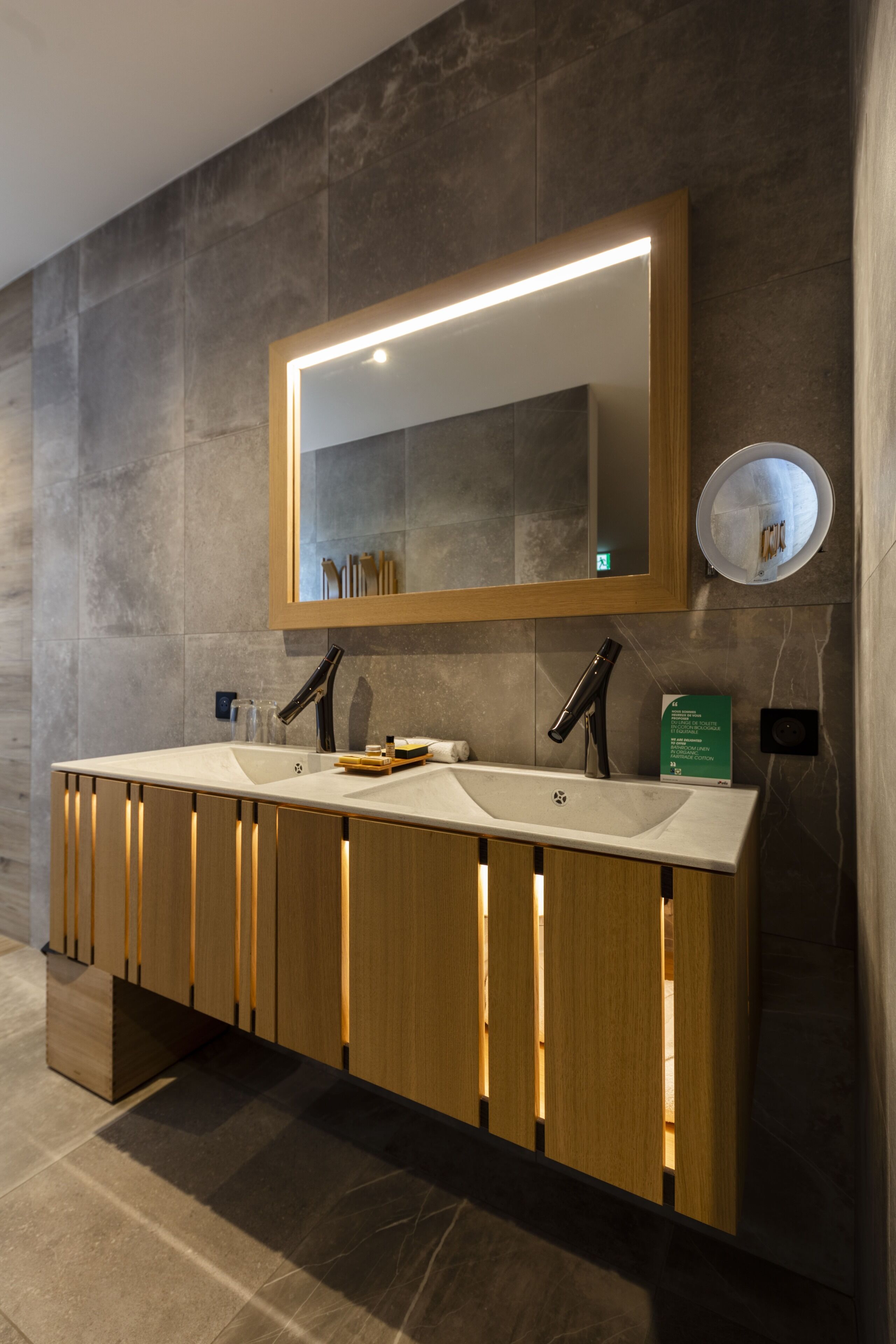 Un baño moderno con tocador doble, un espejo grande e iluminación empotrada en la pared.