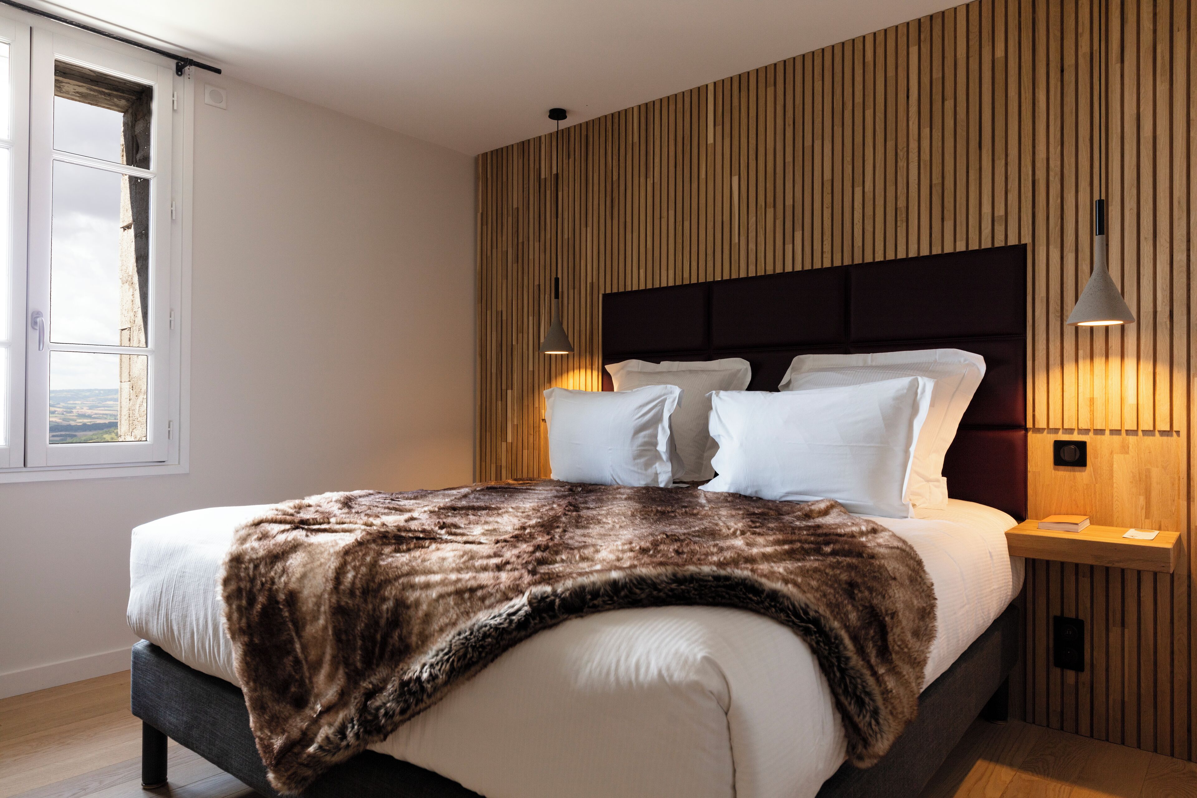 A modern bedroom with a large bed, wooden panel wall, and two bedside lamps.