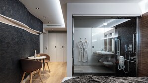 A modern hotel room with a large bed, a glass shower enclosure, a seating area with a table and chairs, and a wardrobe with a mirror. -  Hôtel & Restaurant Origines par Adrien Descouls - Teritoria (Le Broc)