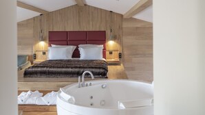 A modern bedroom with a large white bathtub, a wooden ceiling, and a red headboard. -  Hôtel & Restaurant Origines par Adrien Descouls - Teritoria (Le Broc)