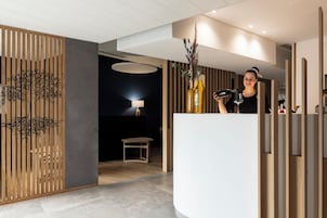 Zona de recepción con diseño moderno, que incluye un panel de madera con diseño de árbol, un mostrador de recepción blanco y una lámpara al fondo.