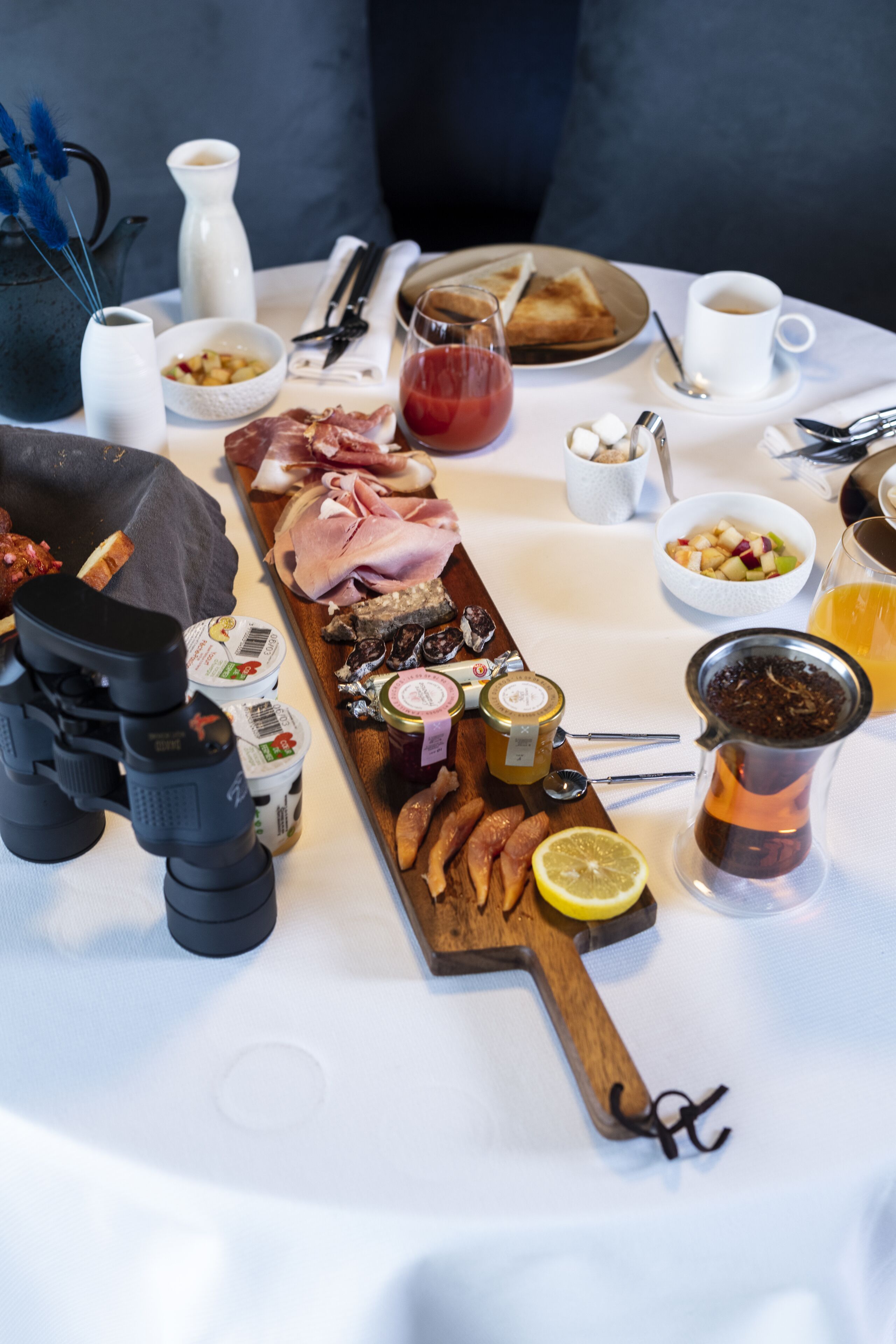 Una mesa de desayuno con una variedad de alimentos, como carnes, quesos y frutas, junto con salsas y bebidas.