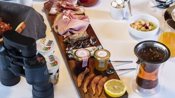 Una mesa de desayuno con una variedad de alimentos, como carnes, quesos y frutas, junto con salsas y bebidas.