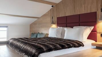 Un dormitorio moderno con techo inclinado de madera, una cama grande con ropa de cama blanca y roja, y una mesita de noche de madera.
