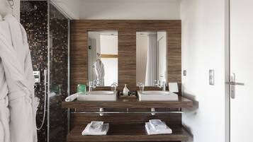 Un baño moderno con dos lavamanos, cabina de ducha de vidrio y tocador de madera.