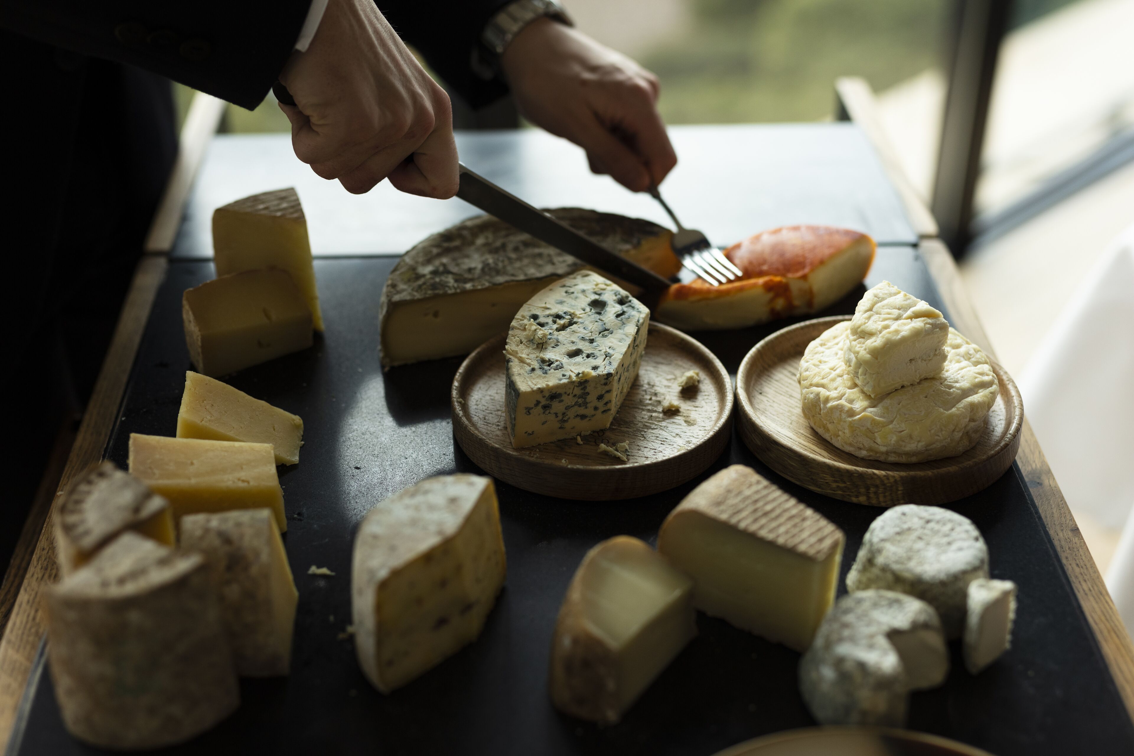 Une sélection de fromages présentés sur une planche en bois, avec une personne qui utilise un couteau et une fourchette.